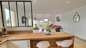 A modern kitchen with a wooden countertop, two white bar stools, a coffee machine, and a view of the outdoor patio area. - du Talbert - Pleubian (PLEUBIAN)