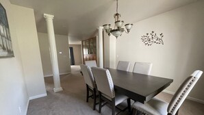 A dining area with a dark wooden table, four upholstered chairs, a chandelier, and a decorative wall piece. - Spacious and Peaceful (College Place)