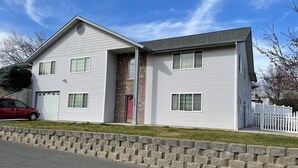 A two-story house with a garage, a brick section, and a white picket fence. - Spacious and Peaceful (College Place)