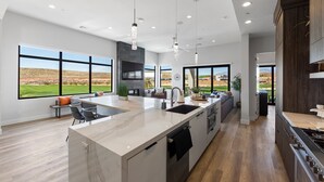 Une cuisine moderne dotée d’un grand îlot central, d’appareils électroménagers intégrés et de grandes fenêtres offrant une vue sur l’extérieur.