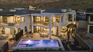 Une maison moderne à plusieurs étages, dotée d’une piscine, de grandes fenêtres et offrant une vue sur les montagnes.