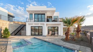 Ein modernes, zweistöckiges Haus mit Swimmingpool, Sitzgelegenheiten im Freien und Palmen.