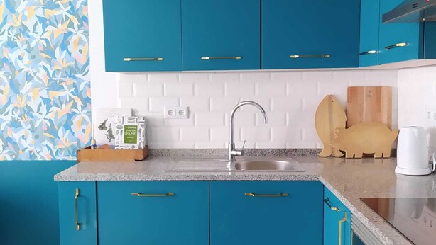 Une cuisine avec des armoires de couleur turquoise, un dosseret blanc, un évier en acier inoxydable et un luminaire suspendu.