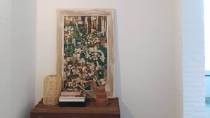 Une pièce avec un mur blanc, une commode en bois, une œuvre d’art encadrée et une étagère contenant divers objets.