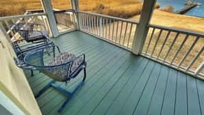 A covered deck with two chairs and a table, overlooking a body of water and marshland.