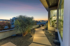 A modern outdoor pathway leading to a building with large windows, surrounded by landscaped areas and a view of the cityscape.