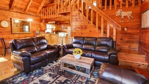 A log cabin interior with two leather sofas, a coffee table with a vase of sunflowers, and a patterned rug. - Escape to Moose Crossing – A Cozy Cabin Retreat in Blue Ridge, GA! (Blue Ridge)