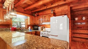 A wooden cabin kitchen with granite countertops, a white refrigerator, wooden cabinets, and a gas stove. - Escape to Moose Crossing – A Cozy Cabin Retreat in Blue Ridge, GA! (Blue Ridge)