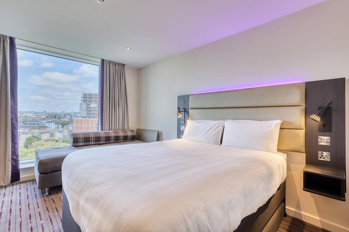 Une chambre d’hôtel avec un grand lit, un canapé, une vue sur la ville et une tête de lit moderne.