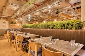 A restaurant with wooden tables, leather booths, hanging pendant lights, and a green plant wall. - Premier Inn London Paddington - Paddington Basin (London)