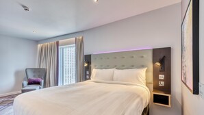 Een moderne hotelkamer met een groot bed, een stoel, een wandplank en een raam met gordijnen.