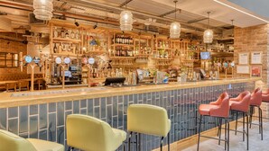 Een bar met een lange toonbank, verschillende barkrukken en een divers aanbod aan flessen en glazen op planken.