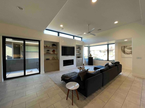 A spacious living area with a large sofa, a flat-screen TV, and a sliding glass door leading to a balcony.