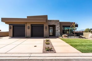 A modern two-story house with a garage, a well-maintained lawn, and a clear sky.