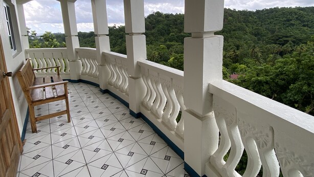 Un balcon avec un banc en bois, des balustrades blanches et un sol carrelé.