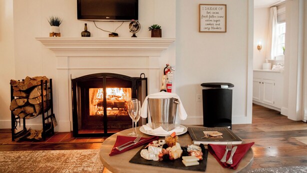 A cozy living room with a fireplace, a dining table set for a meal, and a kitchen in the background.