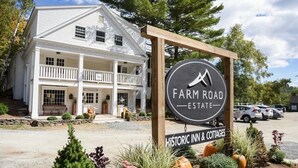 A two-story white building with a porch, labeled "Farm Road Estate Historic Inn & Cottages."