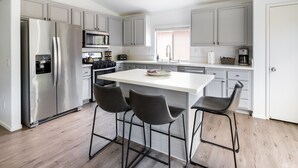 Una cocina moderna con una isla central, electrodomésticos de acero inoxidable y taburetes de bar.