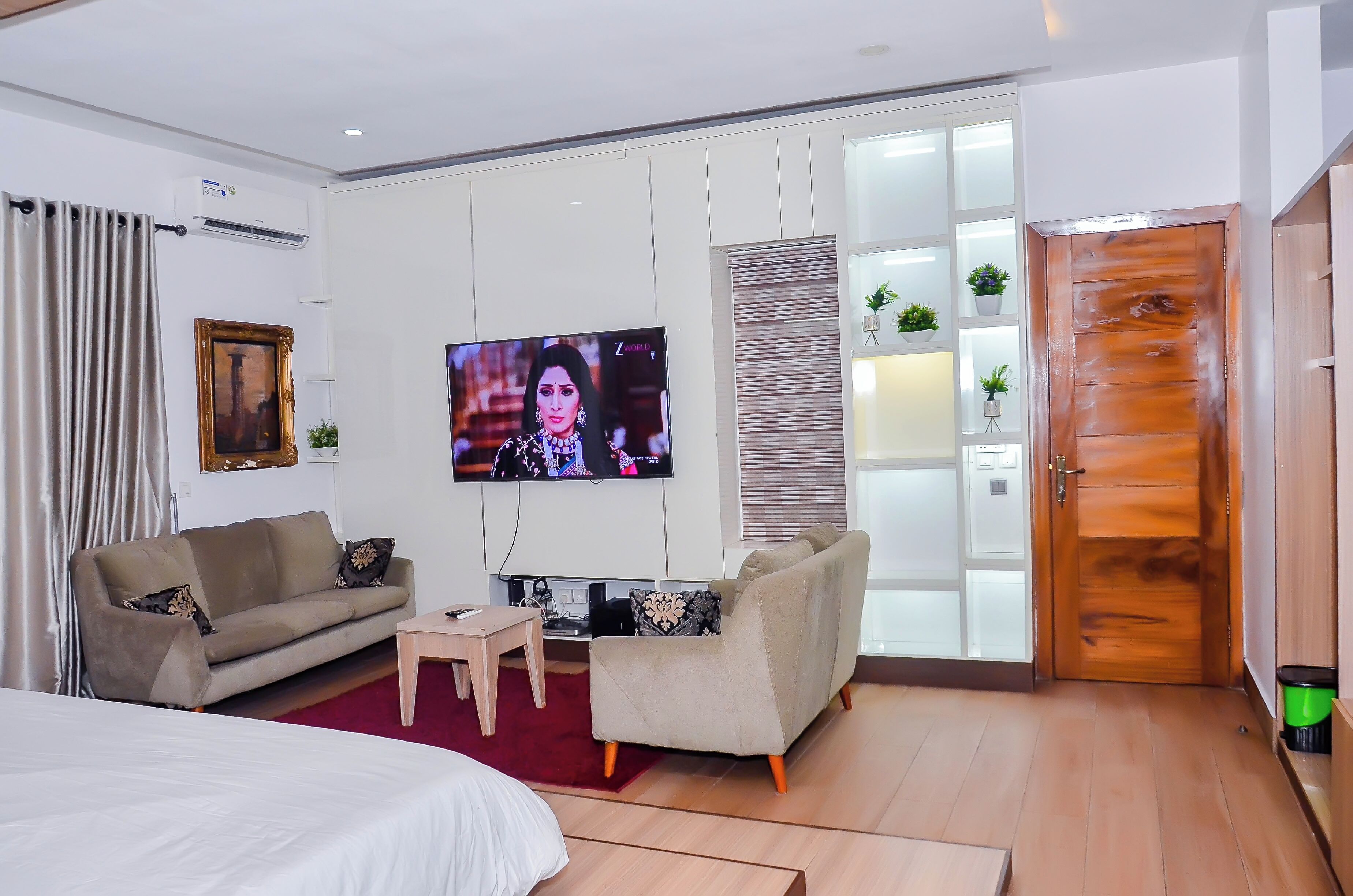 A modern hotel room with a sofa, a TV, a wooden door, and a small table.