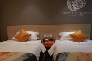 Two single beds with white mattresses and pillows, a nightstand with a telephone and power outlet, and a simple design.