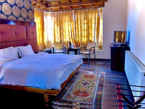 A hotel room with a bed, a desk with a chair, a television, and a window with curtains. - Hotel Spic N Span (Leh)
