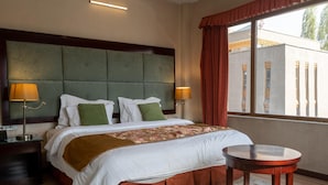 Hotellihuone, jossa on suuri sänky, kaksi yöpöytävalaisinta, pyöreä pöytä ja ikkuna, jossa on verhot.