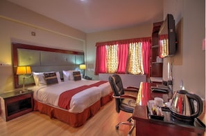 A hotel room with a large bed, a desk with a chair, a TV, and a radiator. - Hotel Spic N Span (Leh)