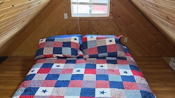 A loft bedroom with a wooden sloped ceiling, a single window, and a bed with a patchwork quilt.