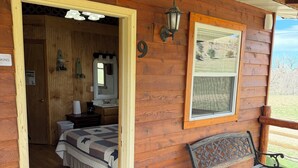 Une cabane en bois comprenant une chambre, un banc et offrant une vue sur l’extérieur.