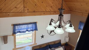 Une chambre avec un plafond en bois, un lit recouvert d’une courtepointe, une table de chevet avec une lampe et une fenêtre avec un rideau.