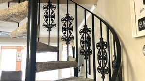 Una escalera de caracol con barandilla beige alfombrada y balaustradas de hierro forjado negro.