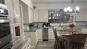 Cocina moderna con armarios blancos, horno empotrado y zona de comedor de madera con una isla central.