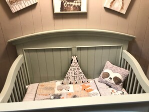 A crib with a green headboard, a pillow with a message, and a blanket with animal prints. - Relax on the edge of Little Red @ Griffin Little Red River Cabin (Heber Springs)