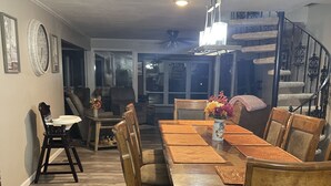 Un comedor con una mesa y sillas de madera, una araña y una escalera al fondo.