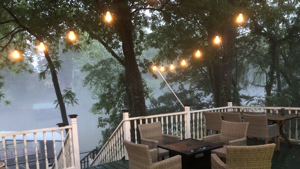 Una terraza con mobiliario de mimbre, una mesa y luces colgantes.