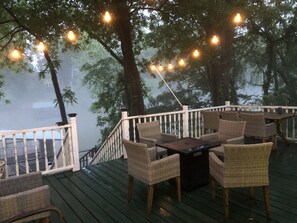 A deck with wicker furniture, a table, and string lights. - Relax on the edge of Little Red @ Griffin Little Red River Cabin (Heber Springs)