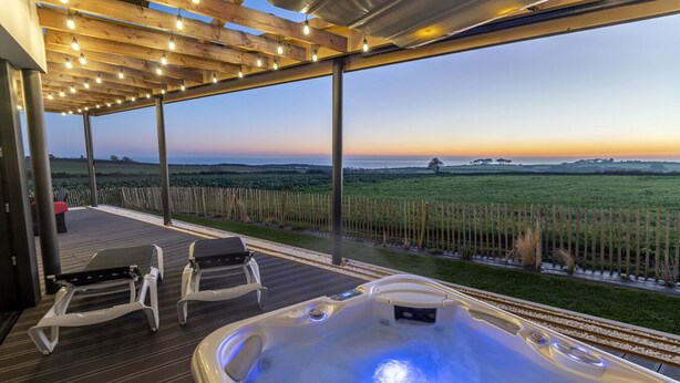 A hot tub with a wooden deck and outdoor seating, overlooking a grassy landscape. - Villa with private Jacuzzi, relaxing wellness weekends and holidays, seaside (Plougonvelin)