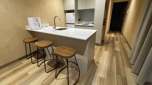 Una cocina pequeña con encimera blanca, un lavamanos y tres taburetes de madera.