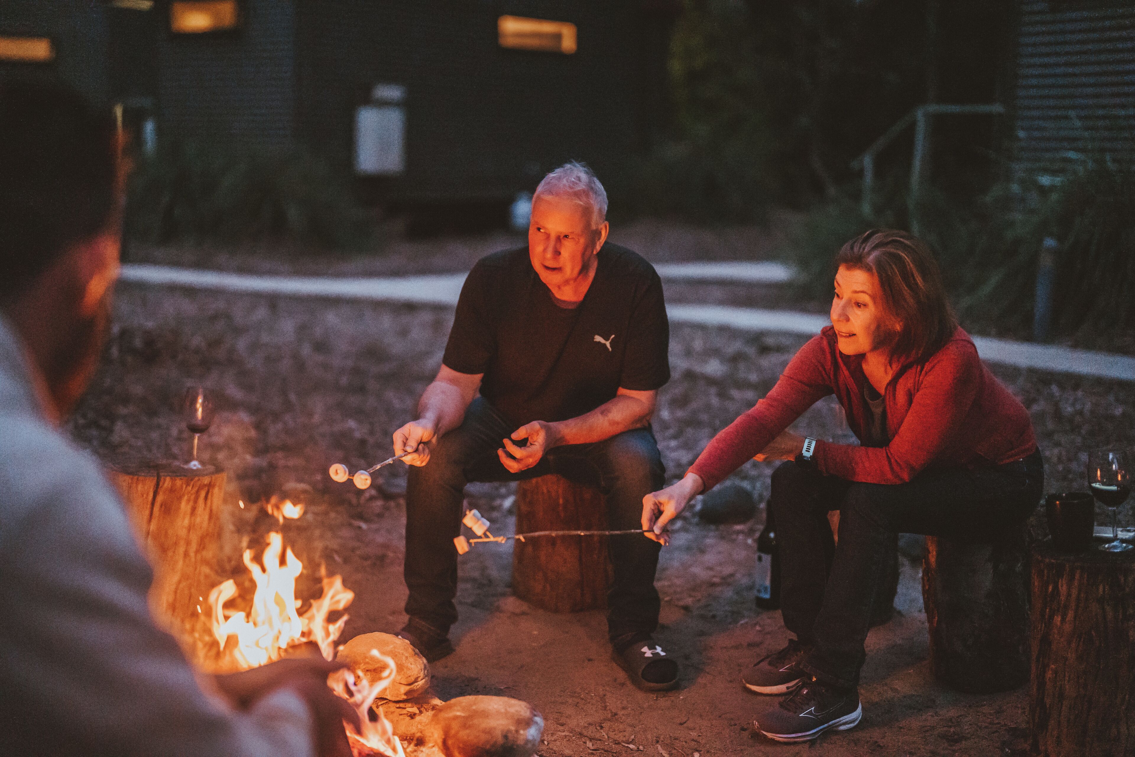 Three people roasting marshmallows around a campfire.