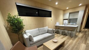 Una sala de estar moderna con un sofá, una mesa de centro, una planta y una cocina con taburetes.