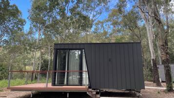 A modern, dark-colored cabin with a glass door and a small deck area.