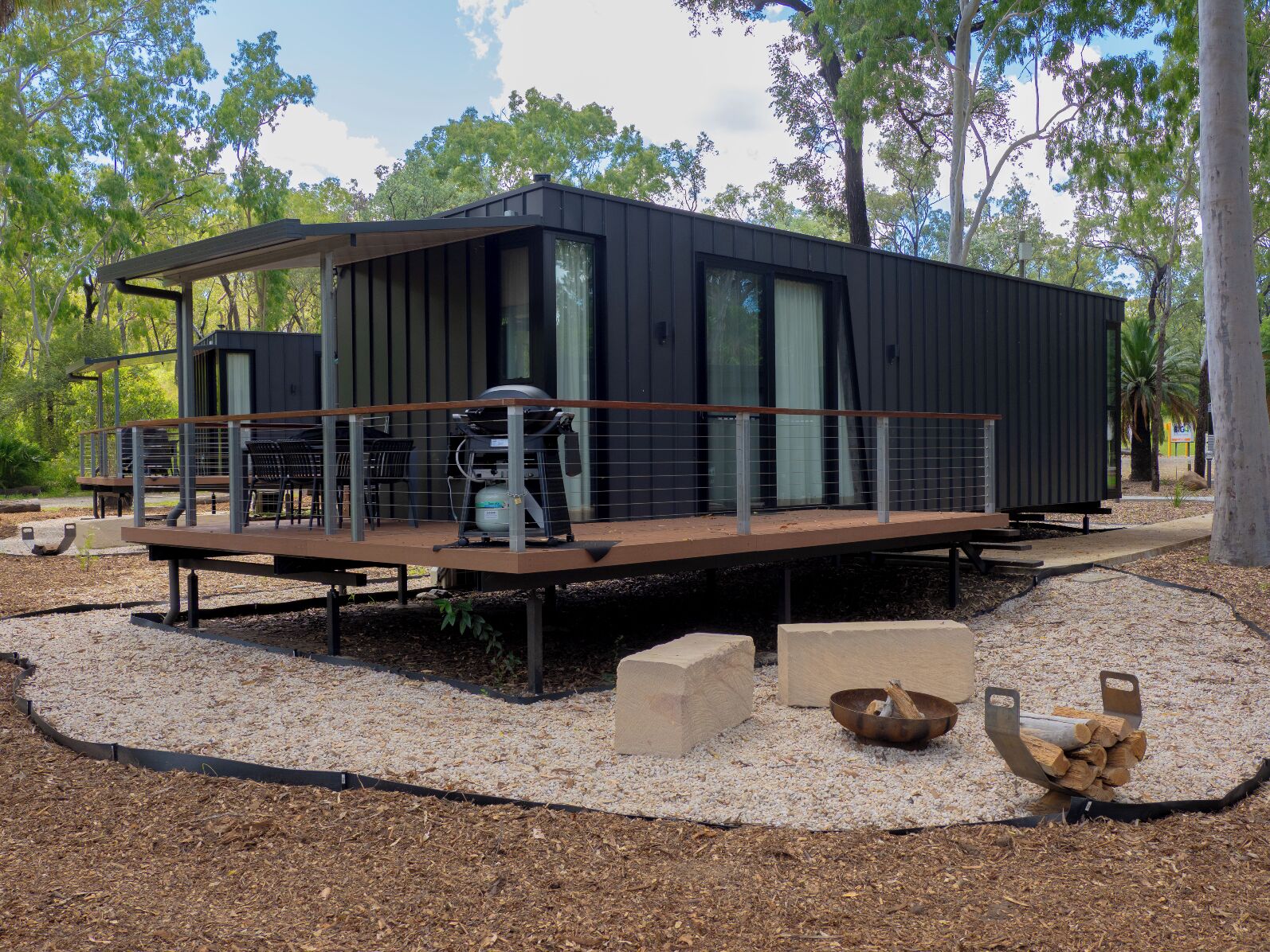 A modern cabin with a deck, outdoor seating, and a barbecue area.