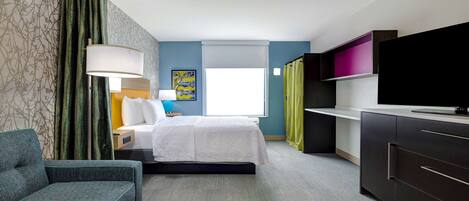 Una habitación de hotel con cama, sofá, televisión, escritorio y ventana.