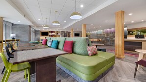 A modern hotel lobby with a green sofa, wooden pillars, and a reception desk. - Home2 Suites by Hilton Wilkes-Barre (Wilkes-Barre)