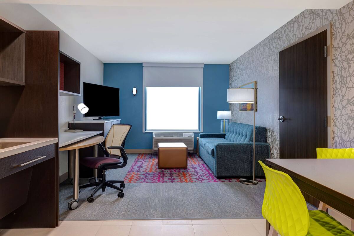 A modern hotel room with a desk, chair, sofa, and a dining table.