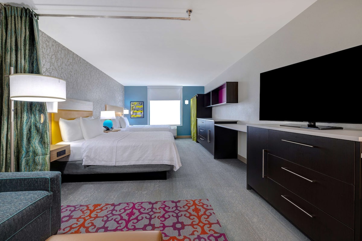 A modern hotel room with a bed, bedside tables, a TV, and a desk.