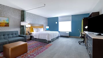 A hotel room with a bed, a sofa, a desk, a television, and a window.