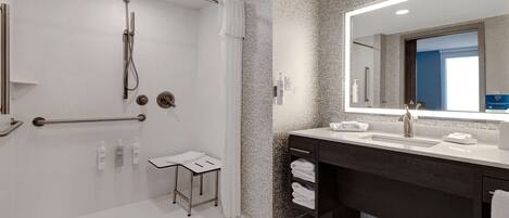 Un baño moderno con cabina de ducha, un espejo grande y un mueble de tocador de madera oscura.