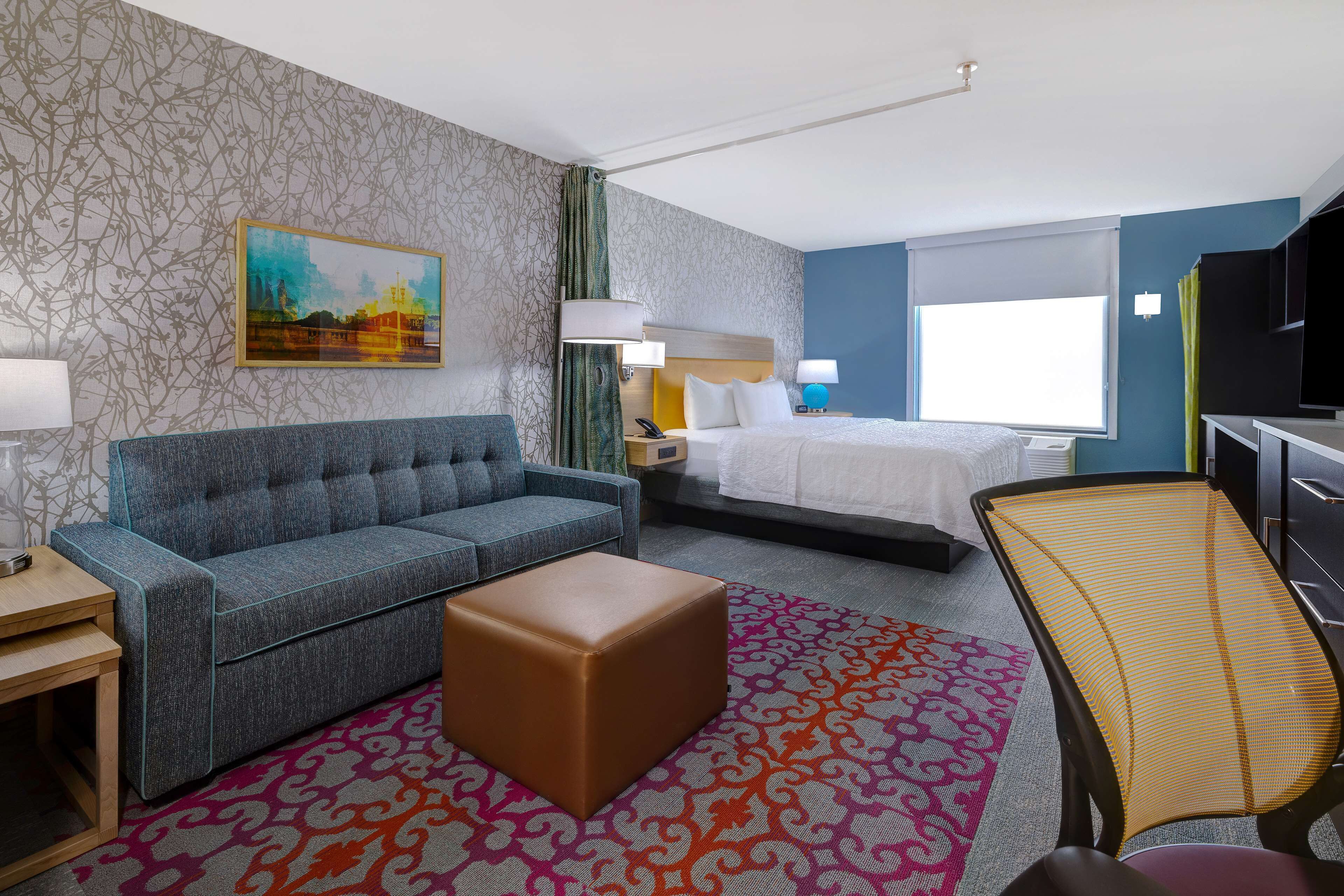 A hotel room with a sofa, a bed, a desk, a chair, and a TV.