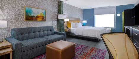 A hotel room with a sofa, a bed, a desk, a chair, and a TV.